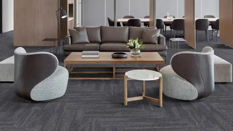 مساحة مكتبية أنيقة تتميز بأرضية مغطاة ببلاطات الموكيت ذات اللون الرمادي الداكن، تتناغم الأثاث الجلدي الفاخر والطاولات الخشبية مع الأرضية الموكيتية، مما يعزز من جمالية وأناقة التصميم الداخلي.